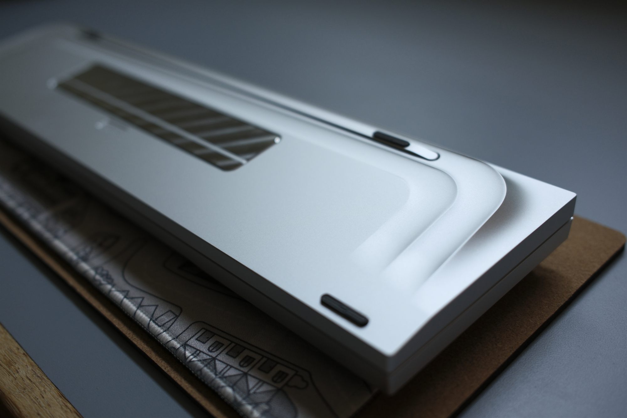 INN FloAT, three-quarter rear view — silver anodized case with navy GMK Striker 2 keycaps and a brushed weight