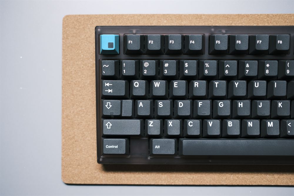 Top-left corner with the teal novelty keycap against the smoke case
